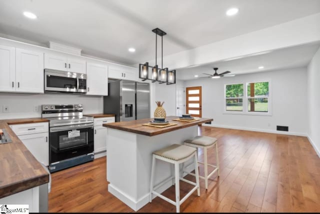 kitchen featuring white cabinetry, appliances with stainless steel finishes, wooden counters, and a kitchen bar