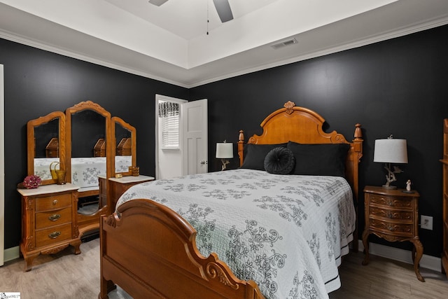 bedroom with a ceiling fan, visible vents, a raised ceiling, baseboards, and light wood-style flooring
