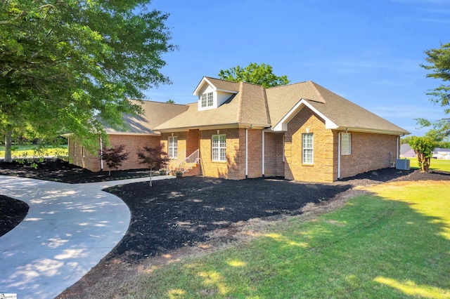 view of front of home with brick siding, a shingled roof, a front yard, and cooling unit