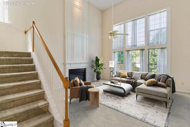 carpeted living room featuring a ceiling fan, a glass covered fireplace, a high ceiling, and stairway