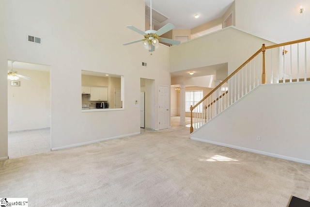 unfurnished living room with visible vents, ceiling fan, and a high ceiling
