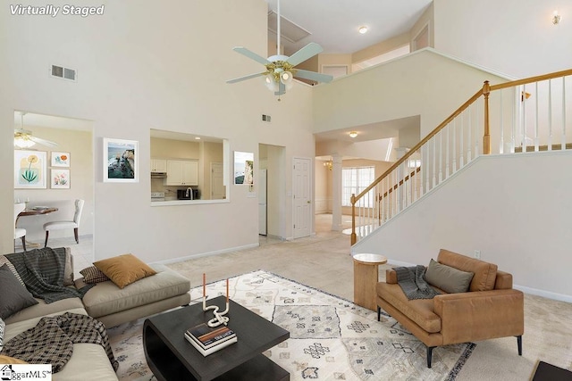 living area featuring stairs, a ceiling fan, a high ceiling, and visible vents