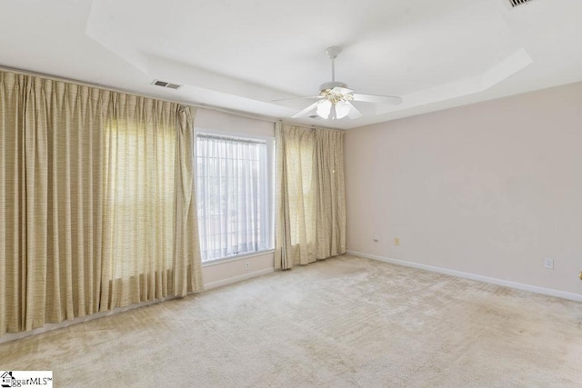 carpeted spare room with visible vents, a ceiling fan, baseboards, and a tray ceiling