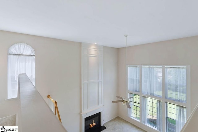 unfurnished living room with a ceiling fan, a glass covered fireplace, and light carpet