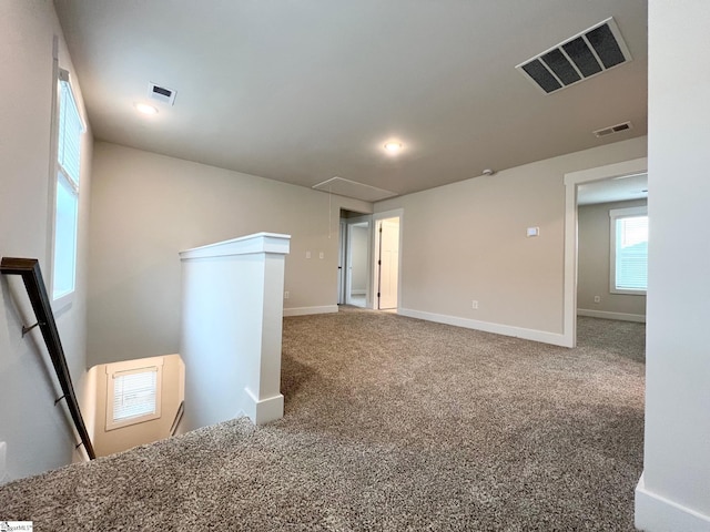 carpeted empty room with baseboards, attic access, and visible vents