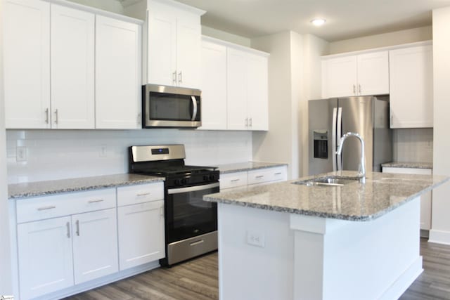 kitchen featuring backsplash, appliances with stainless steel finishes, a center island with sink, dark wood finished floors, and white cabinetry