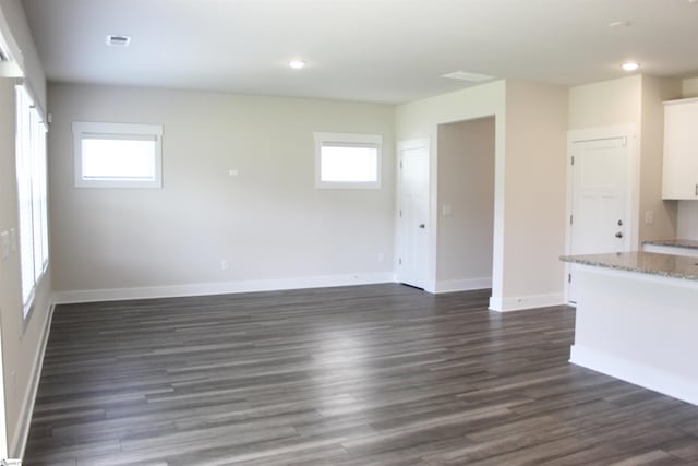 unfurnished living room featuring plenty of natural light, dark wood-style flooring, baseboards, and visible vents