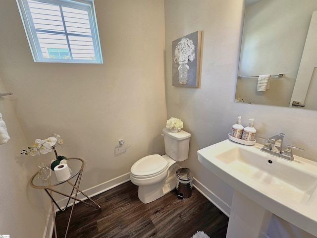 half bath with baseboards, a sink, wood finished floors, and toilet