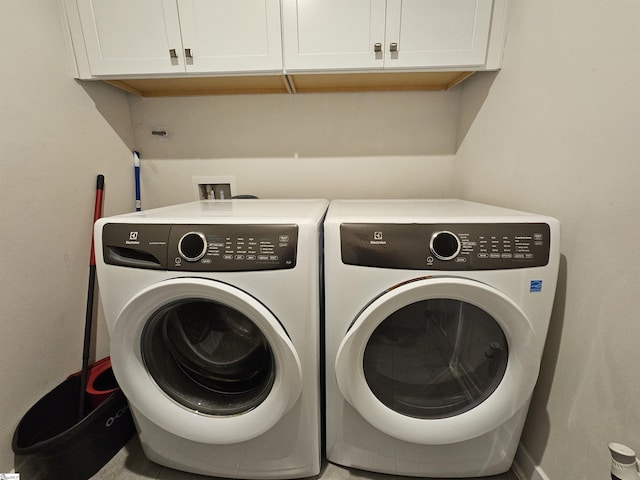clothes washing area featuring baseboards, washer and clothes dryer, and cabinet space