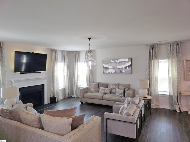 living room with baseboards, a fireplace with raised hearth, and dark wood-style flooring