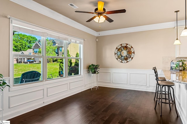 unfurnished dining area featuring a ceiling fan, visible vents, a wainscoted wall, ornamental molding, and dark wood-type flooring