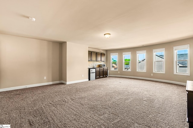 unfurnished living room featuring baseboards, bar area, and carpet