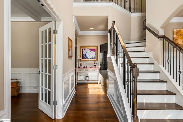 staircase with crown molding, a wainscoted wall, arched walkways, and wood finished floors