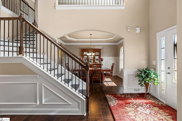 entryway with a towering ceiling, arched walkways, wood finished floors, an inviting chandelier, and a decorative wall