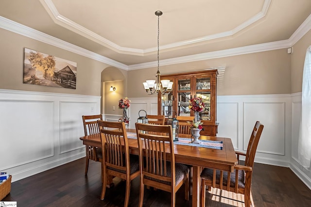 dining space featuring dark wood-style flooring, arched walkways, a raised ceiling, a chandelier, and a decorative wall