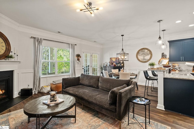 living room featuring an inviting chandelier, a decorative wall, a glass covered fireplace, and dark wood-style floors