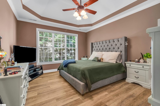 bedroom with crown molding, a raised ceiling, light wood-style floors, baseboards, and visible vents