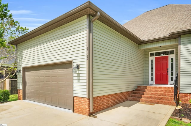 entrance to property featuring roof with shingles, concrete driveway, a garage, and brick siding