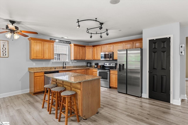 kitchen with a kitchen island, a ceiling fan, a sink, stainless steel appliances, and light wood-style flooring