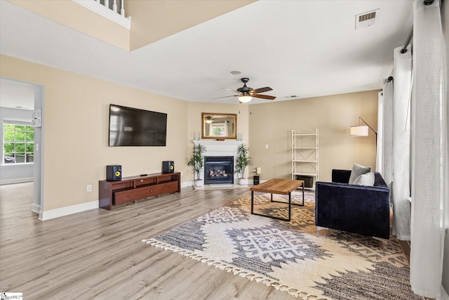 living area with ceiling fan, a glass covered fireplace, baseboards, wood finished floors, and visible vents