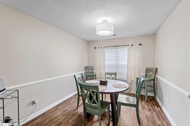 dining space featuring baseboards, a textured ceiling, visible vents, and wood finished floors