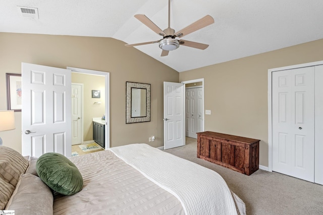 bedroom with ceiling fan, light carpet, visible vents, ensuite bathroom, and vaulted ceiling