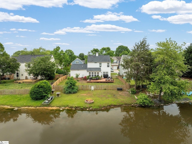 rear view of house featuring a chimney, a deck with water view, a lawn, a fenced backyard, and a fire pit