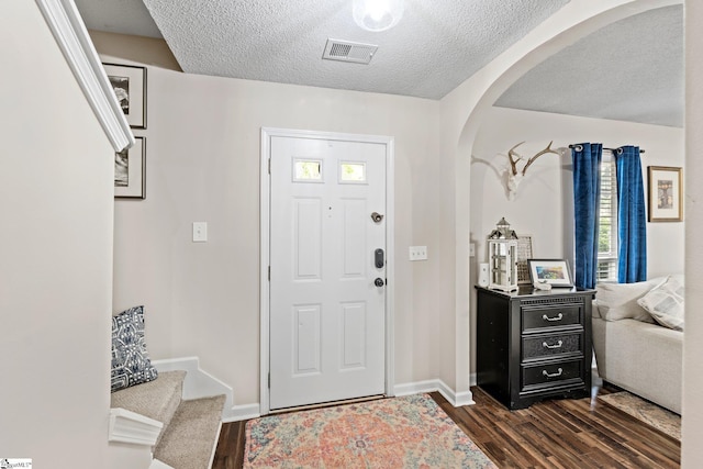 entryway with arched walkways, a textured ceiling, baseboards, dark wood-type flooring, and visible vents