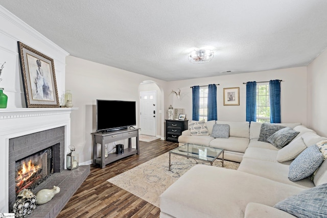 living room featuring a textured ceiling, visible vents, arched walkways, a fireplace, and dark wood-type flooring