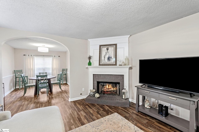 living area featuring wood finished floors, a fireplace, baseboards, a textured ceiling, and arched walkways