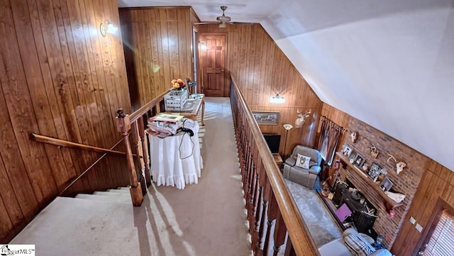 stairway with ceiling fan, carpet, wood walls, and lofted ceiling