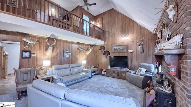 living area with carpet flooring, a ceiling fan, high vaulted ceiling, and wood walls