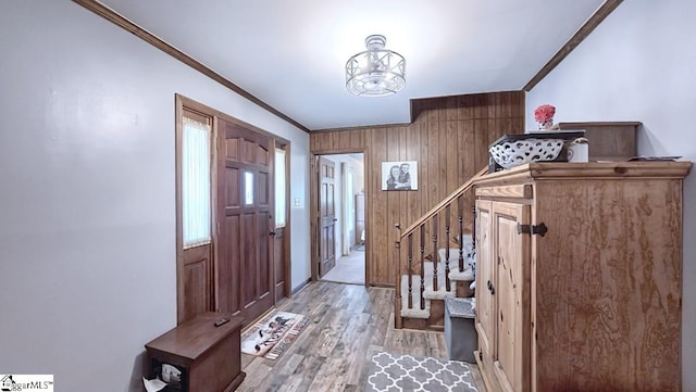 foyer entrance featuring wood walls, an inviting chandelier, ornamental molding, stairs, and light wood-style flooring