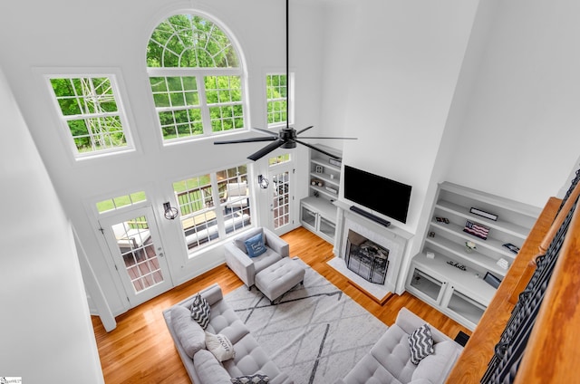 living room with a high ceiling, a fireplace, a ceiling fan, and wood finished floors