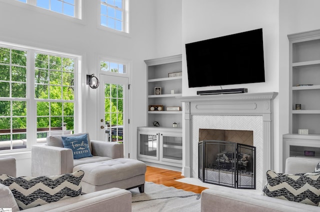 living room featuring a tiled fireplace, a high ceiling, built in features, and wood finished floors