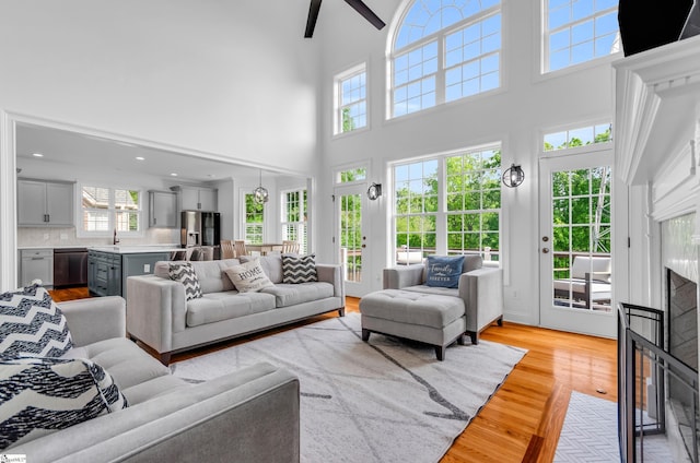 living room with a high ceiling, ceiling fan, a fireplace with flush hearth, and light wood-style flooring