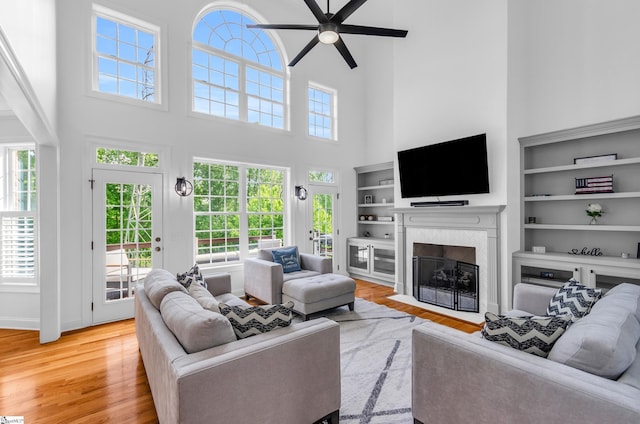 living area featuring a healthy amount of sunlight, a fireplace with flush hearth, wood finished floors, and a towering ceiling