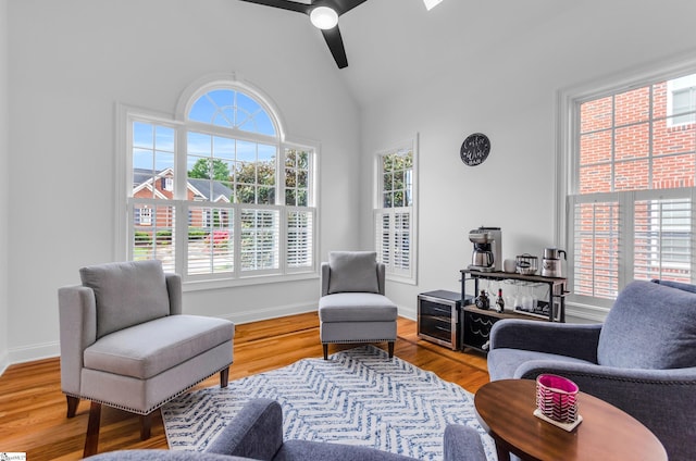 living area with baseboards, ceiling fan, high vaulted ceiling, and wood finished floors