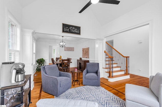 living area featuring high vaulted ceiling, ceiling fan with notable chandelier, wood finished floors, ornamental molding, and stairway
