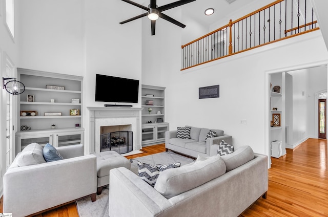 living room featuring a fireplace with flush hearth, a high ceiling, ceiling fan, and wood finished floors