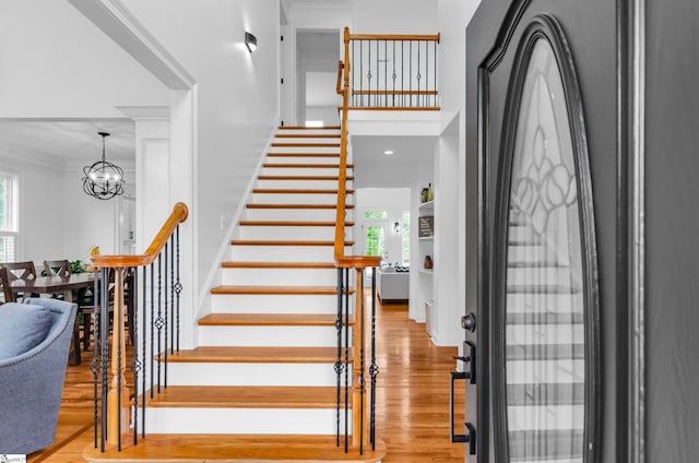 staircase with plenty of natural light, ornamental molding, wood finished floors, and a chandelier
