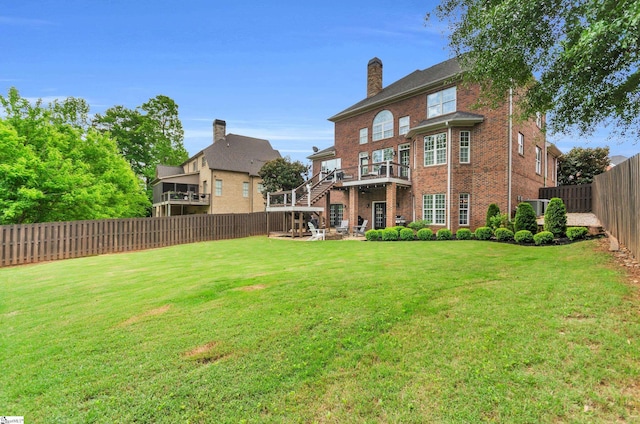 back of house featuring a fenced backyard, a chimney, brick siding, stairs, and a lawn
