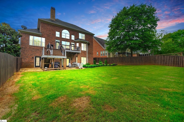 back of house featuring a chimney, brick siding, a fenced backyard, a balcony, and a yard