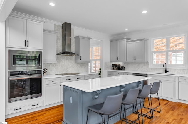 kitchen with wall chimney range hood, tasteful backsplash, a sink, ornamental molding, and stainless steel appliances