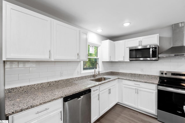 kitchen with wall chimney range hood, white cabinets, a sink, stainless steel appliances, and tasteful backsplash