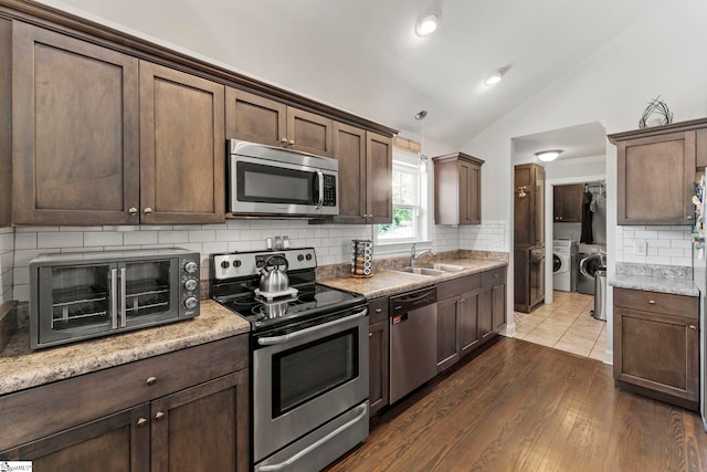 kitchen featuring decorative backsplash, independent washer and dryer, a sink, lofted ceiling, and stainless steel appliances