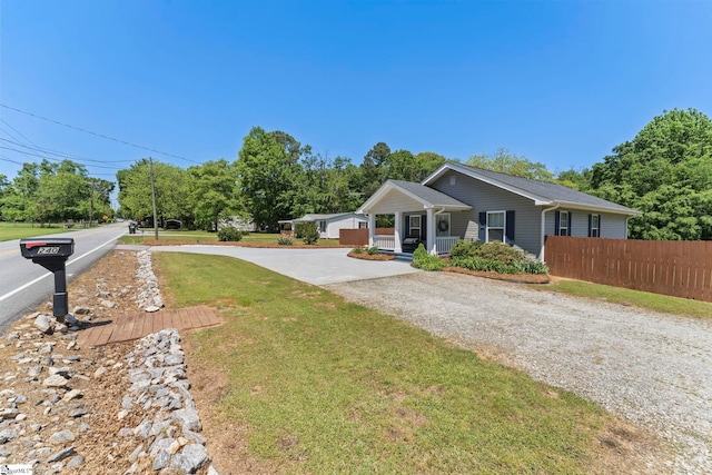 bungalow with covered porch, gravel driveway, fence, and a front lawn