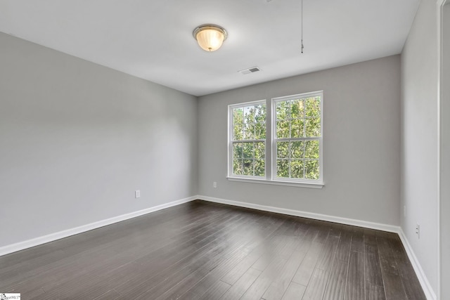 empty room with dark wood-style flooring, baseboards, and visible vents