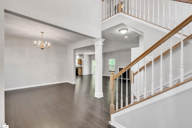interior space featuring a high ceiling, a chandelier, baseboards, wood finished floors, and ornate columns