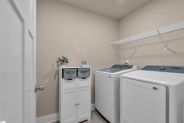 clothes washing area with cabinet space, baseboards, washing machine and dryer, and light tile patterned floors